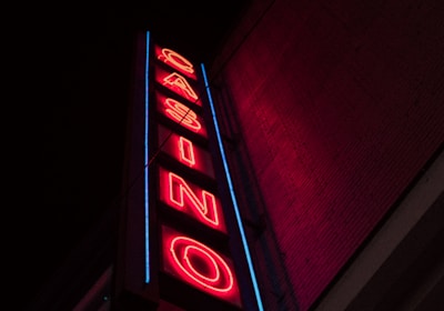 A neon sign is prominently displayed on the side of a building. The sign is vertical and spells out the word 'CASINO' in bold, red neon letters. Surrounding the letters is a blue outline that adds to the vibrancy of the sign against the otherwise dark facade of the building.